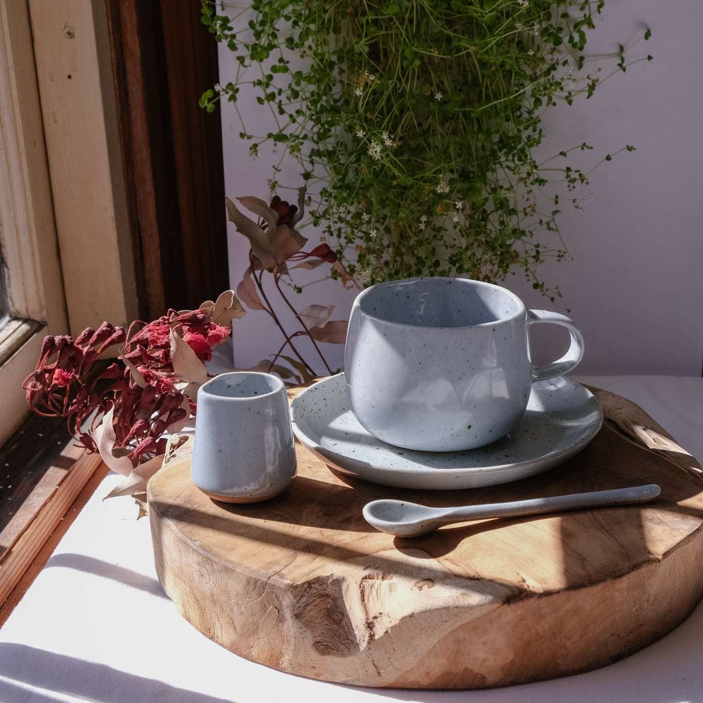 Tea and coffee Ritual Set basking in the sun, a handmade mug, a saucer, a teaspoon and milk pourer all handmade stoneware