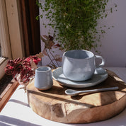 Tea and coffee Ritual Set basking in the sun, a handmade mug, a saucer, a teaspoon and milk pourer all handmade stoneware