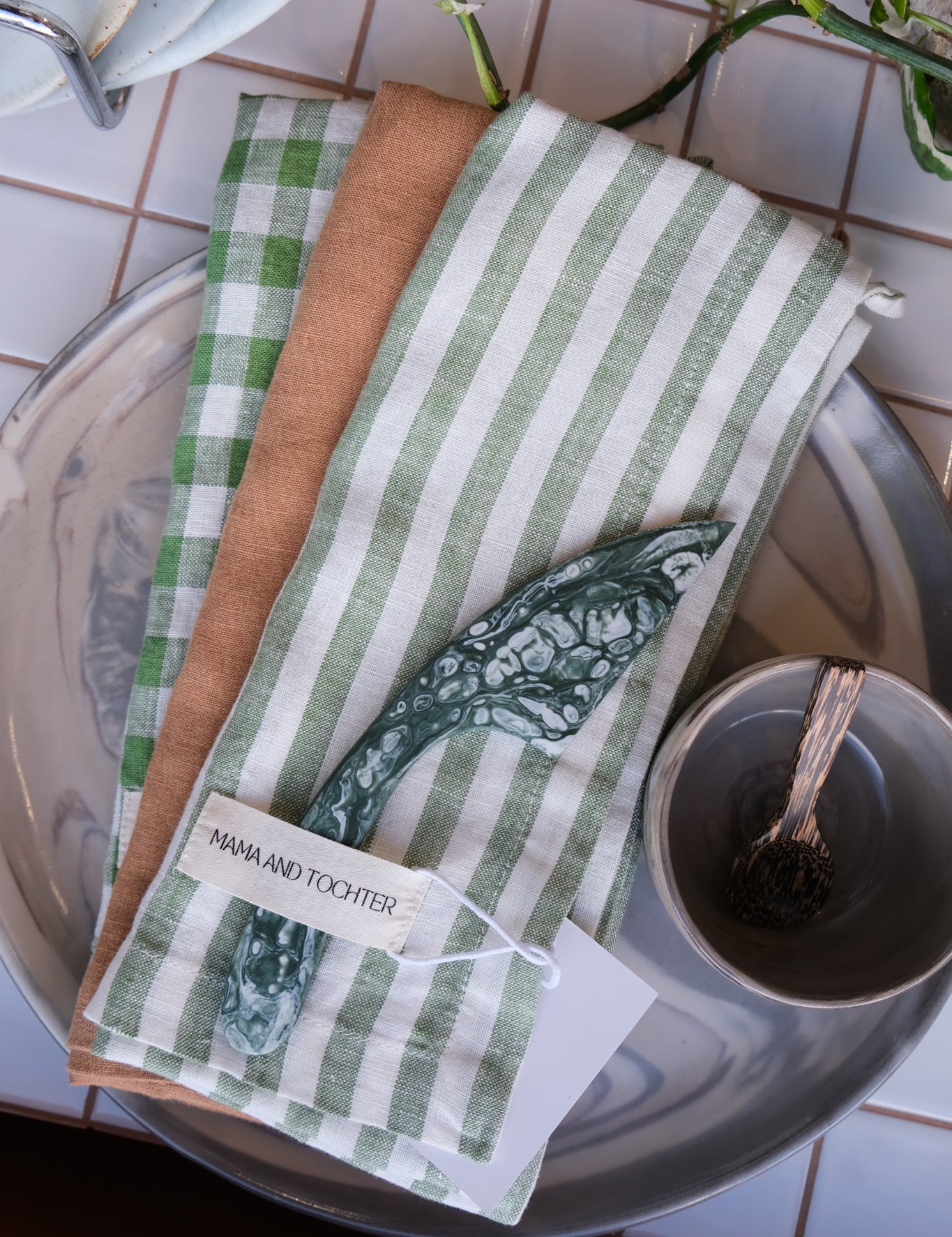 Set of green and white striped tea towels on a tiled surface with a Palinopsia teacup and spoon.