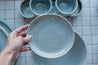 Hand holding a small side plate with speckles in grey blue by Palinopsia Ceramics 