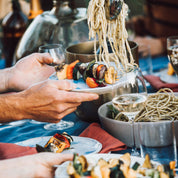Busy dinner table with pasta salad and grilled vegetables on handmade Palinopsia Ceramic plates