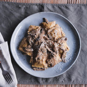 Roast duck ravioli alla boscaiola on a blue dinner plate and Palinopsia linen