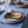 Rustic table setting with ceramic Dinner plate and side plate with olive linen napkin, gold cutlery and a blue tablecloth