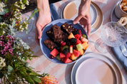 Bright summer outdoor dining table with a handmade blue pottery bowl with fruit and chocolate brownies by Soul Origin and Palinopsia Ceramics dinnerware sets in pink and chocolate
