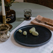 Table setting by  Palinopsia Ceramics displaying their Australian made linen collection of table cloths, placemats and napkins with a black handmade plate and still life setting in Sydney Australia
