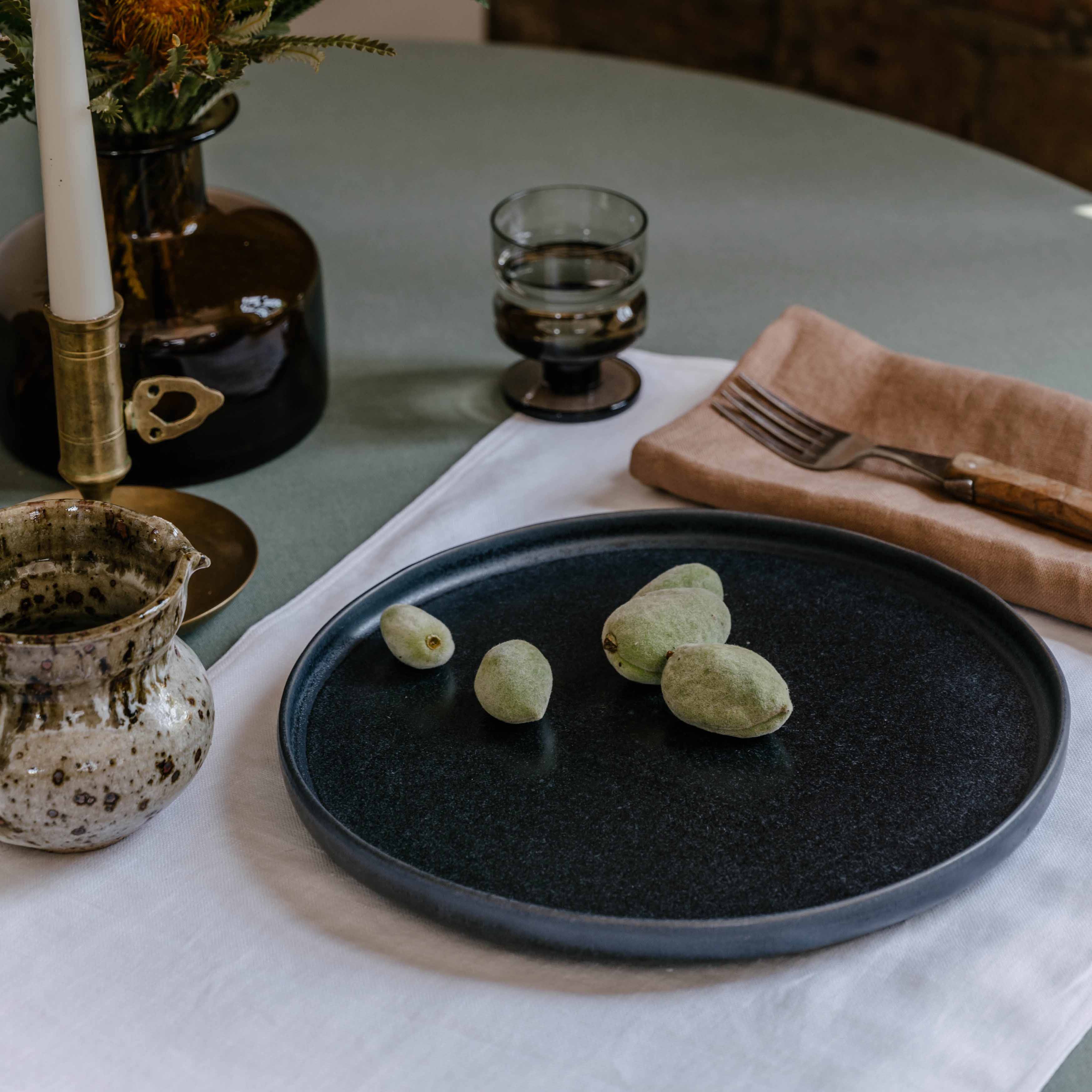 Table setting by  Palinopsia Ceramics displaying their Australian made linen collection of table cloths, placemats and napkins with a black handmade plate and still life setting in Sydney Australia