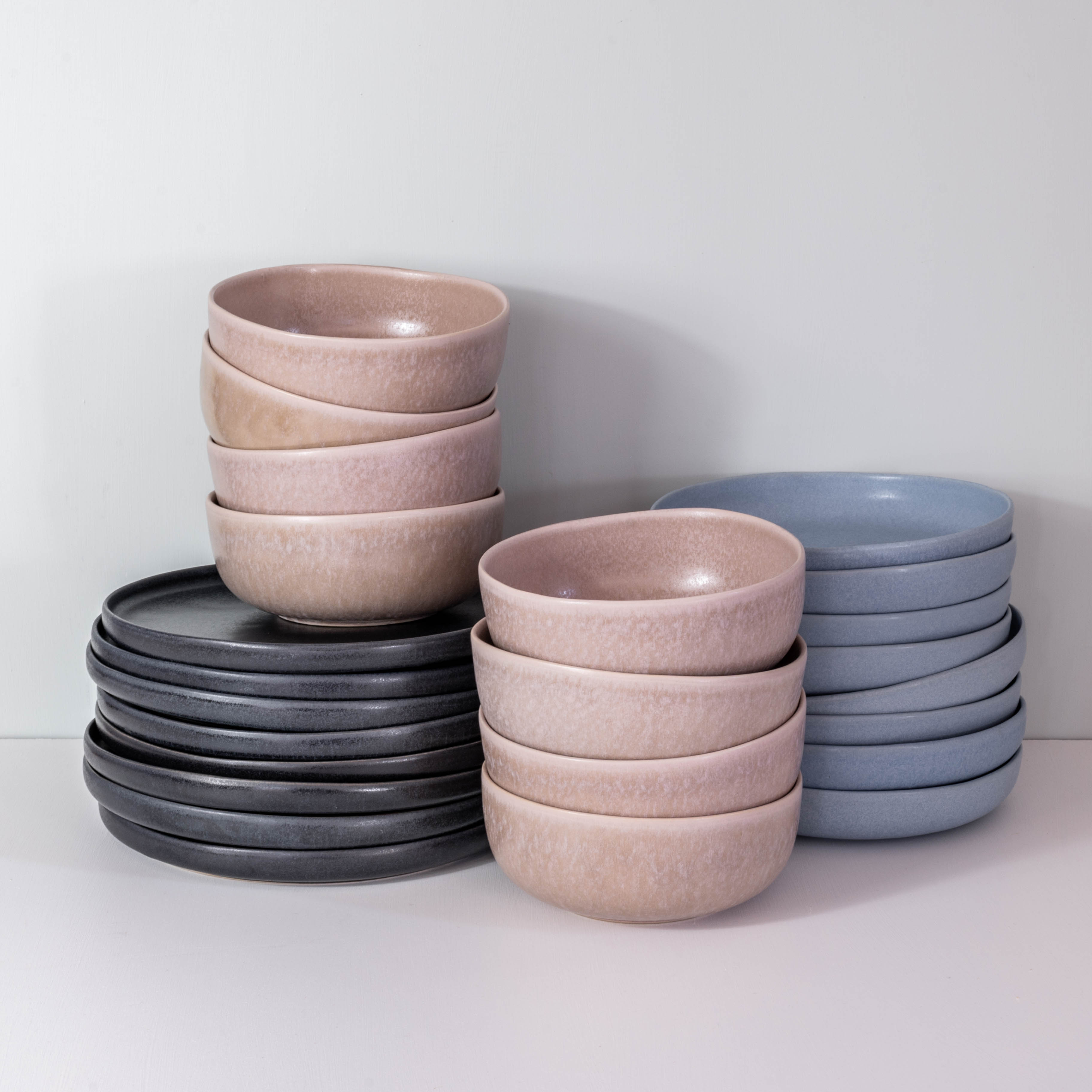 Handmade dinner set by Palinopsia ceramics showing how the pieces are stacked which includes a black dinner plate, blue pasta bowl and a mushroom grey soup bowl