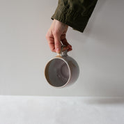 Hand holding a single handmade stoneware mug by Palinopsia Ceramics