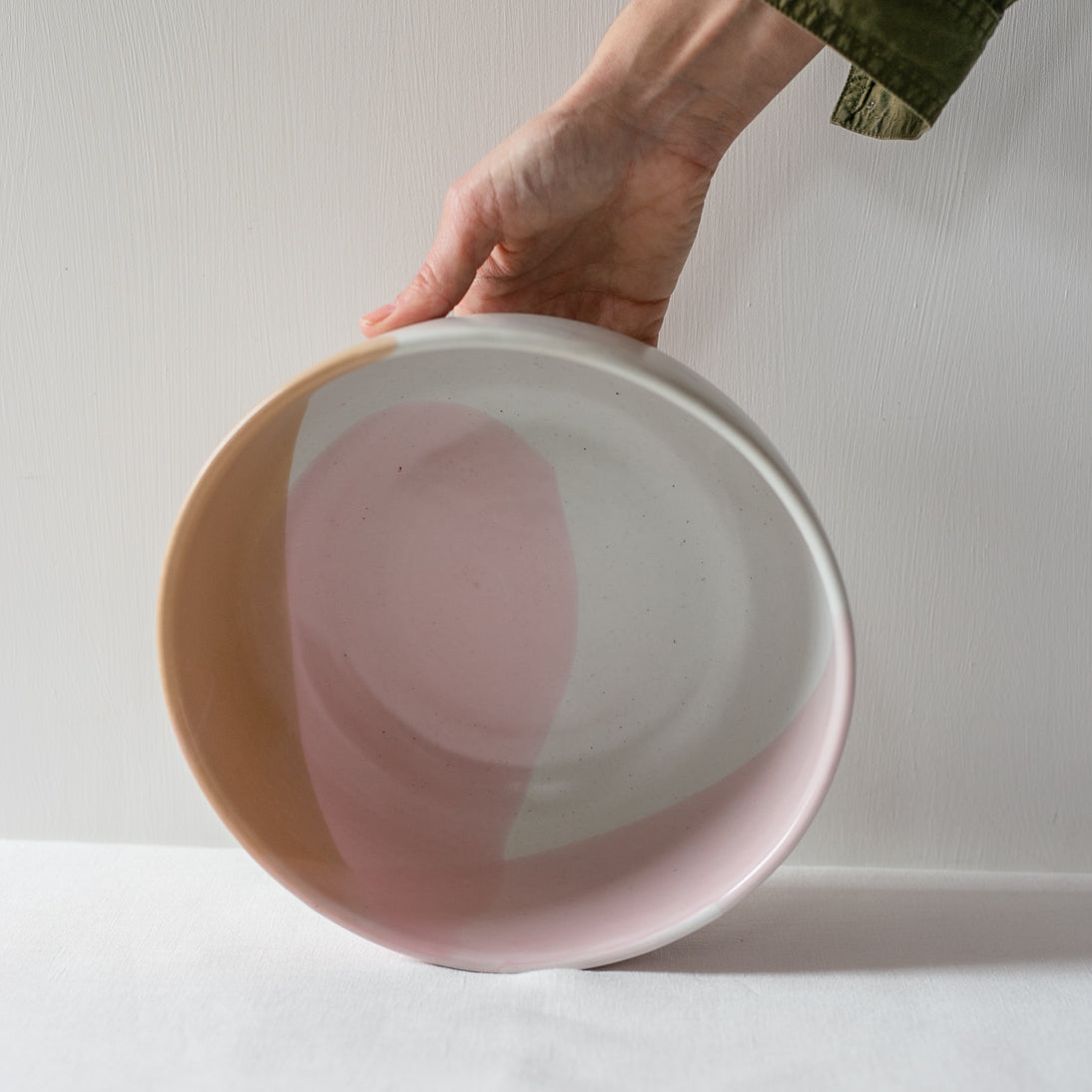 Hand holding a handmade fruit bowl in colourful pink, brown and white playful colours by Palinopsia Ceramics