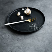 Handmade Black dinner plate by Palinopsia Ceramics in Newcastle with garlic salt in a moody still life setting