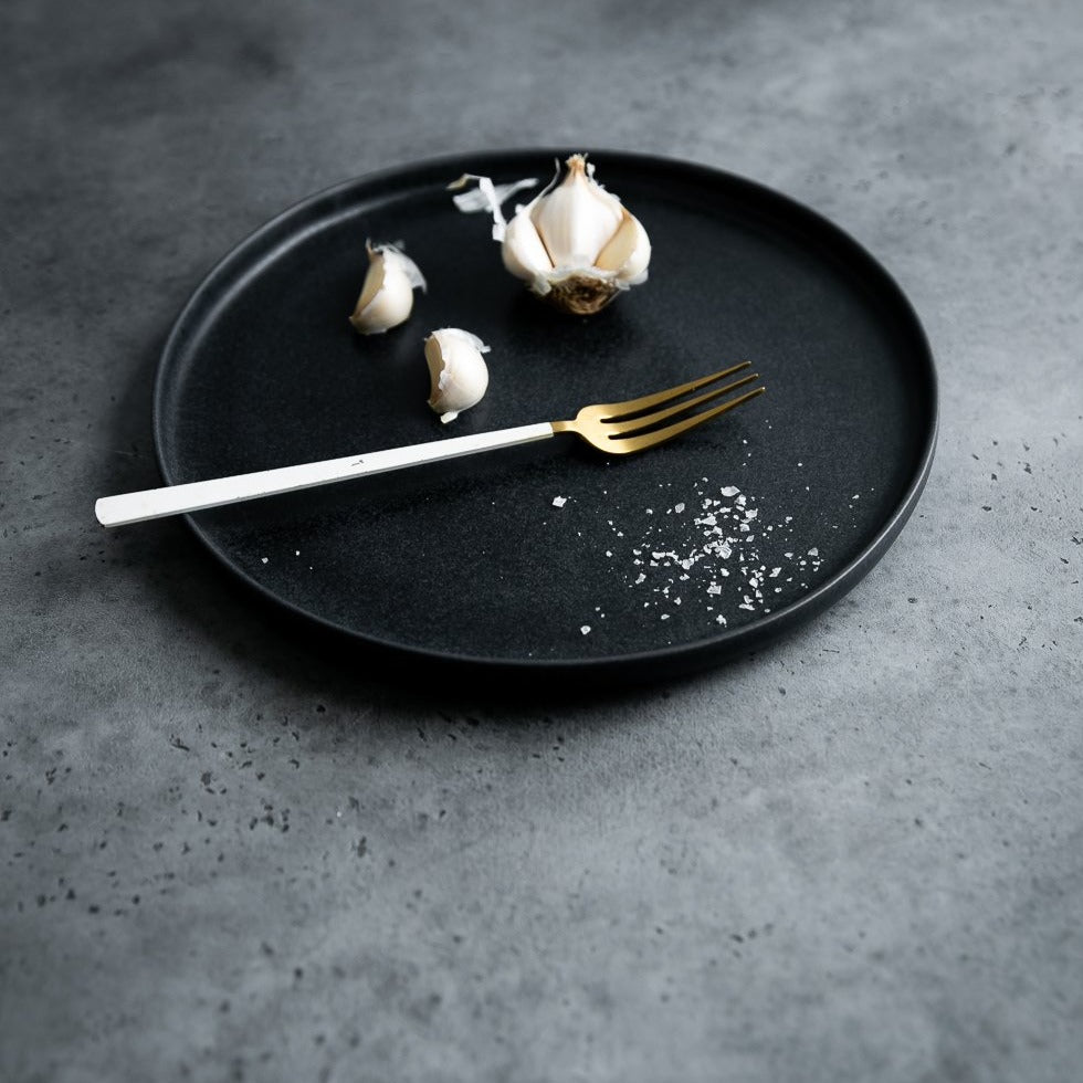 Handmade Black dinner plate by Palinopsia Ceramics in Newcastle with garlic salt in a moody still life setting
