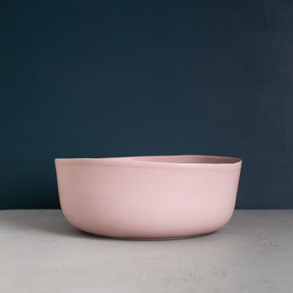 Handmade fruit bowl in dusty pink with organic shape against a navy blue wall by Palinopsia Ceramics in Sydney