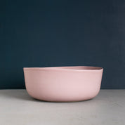 Handmade fruit bowl in dusty pink with organic shape against a navy blue wall by Palinopsia Ceramics in Sydney