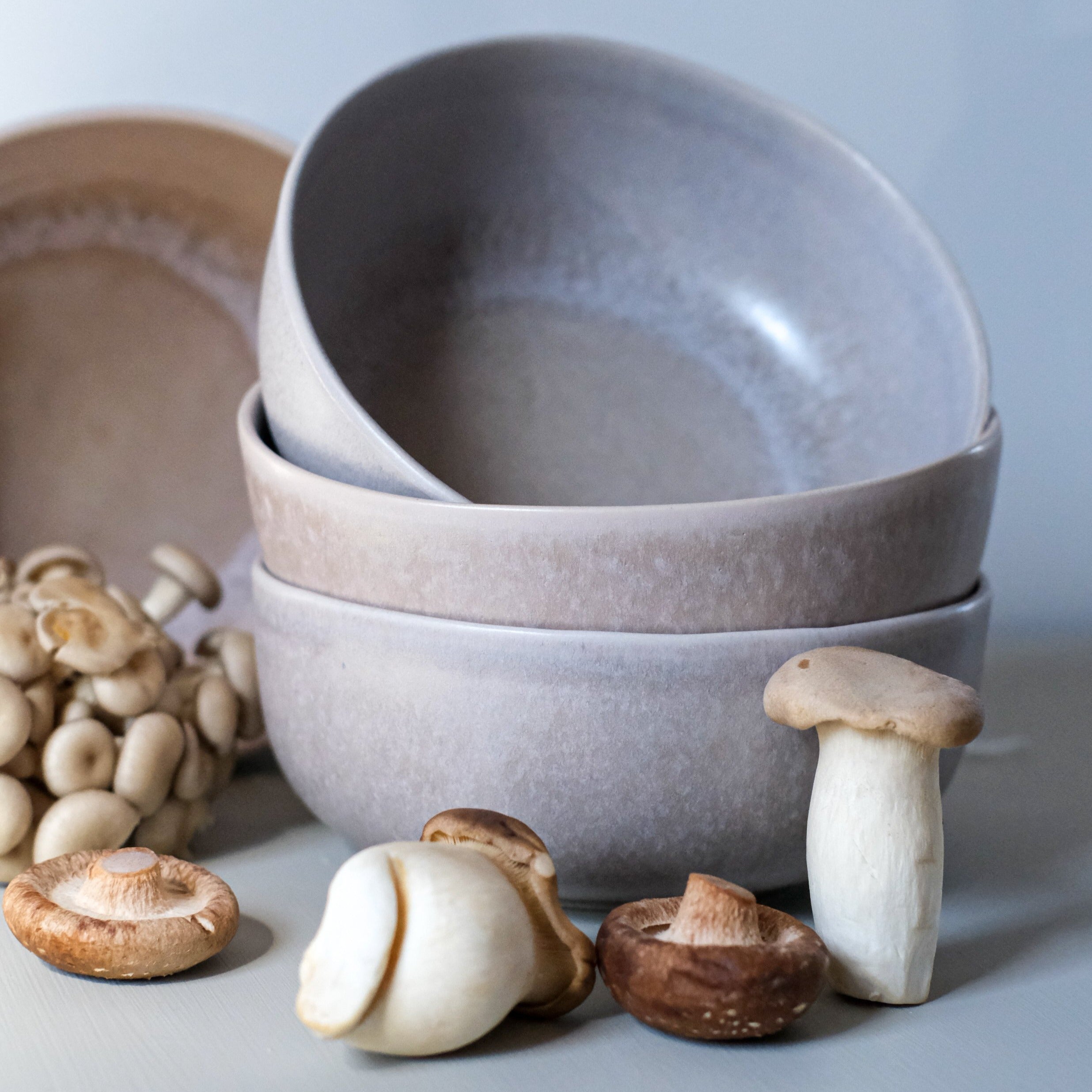 Side view of stacked handmade stoneware soup bowls in a mushroom grey colour styled with Sydney gourmet mushrooms by Palinopsia Ceramics