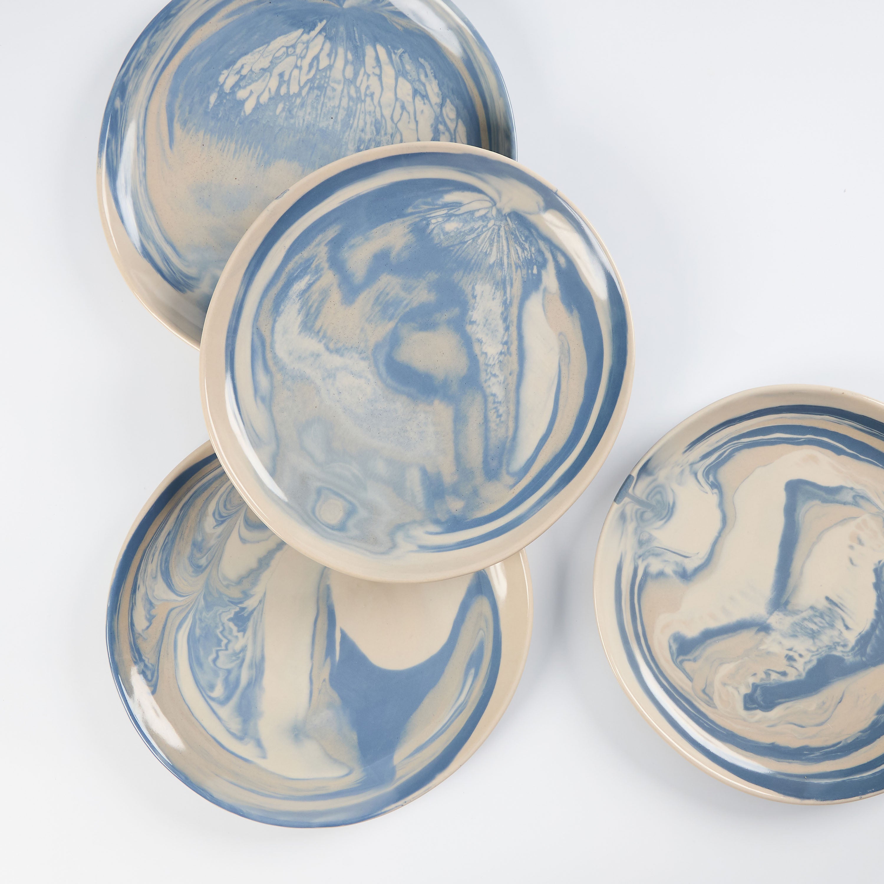 Set of four small handmade ceramic plates with a marbled clay pattern in cobalt blue, beige and cream on a white background by Palinopsia