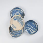 Set of four small handmade ceramic plates with a marbled clay pattern in cobalt blue, beige and cream on a white background by Palinopsia