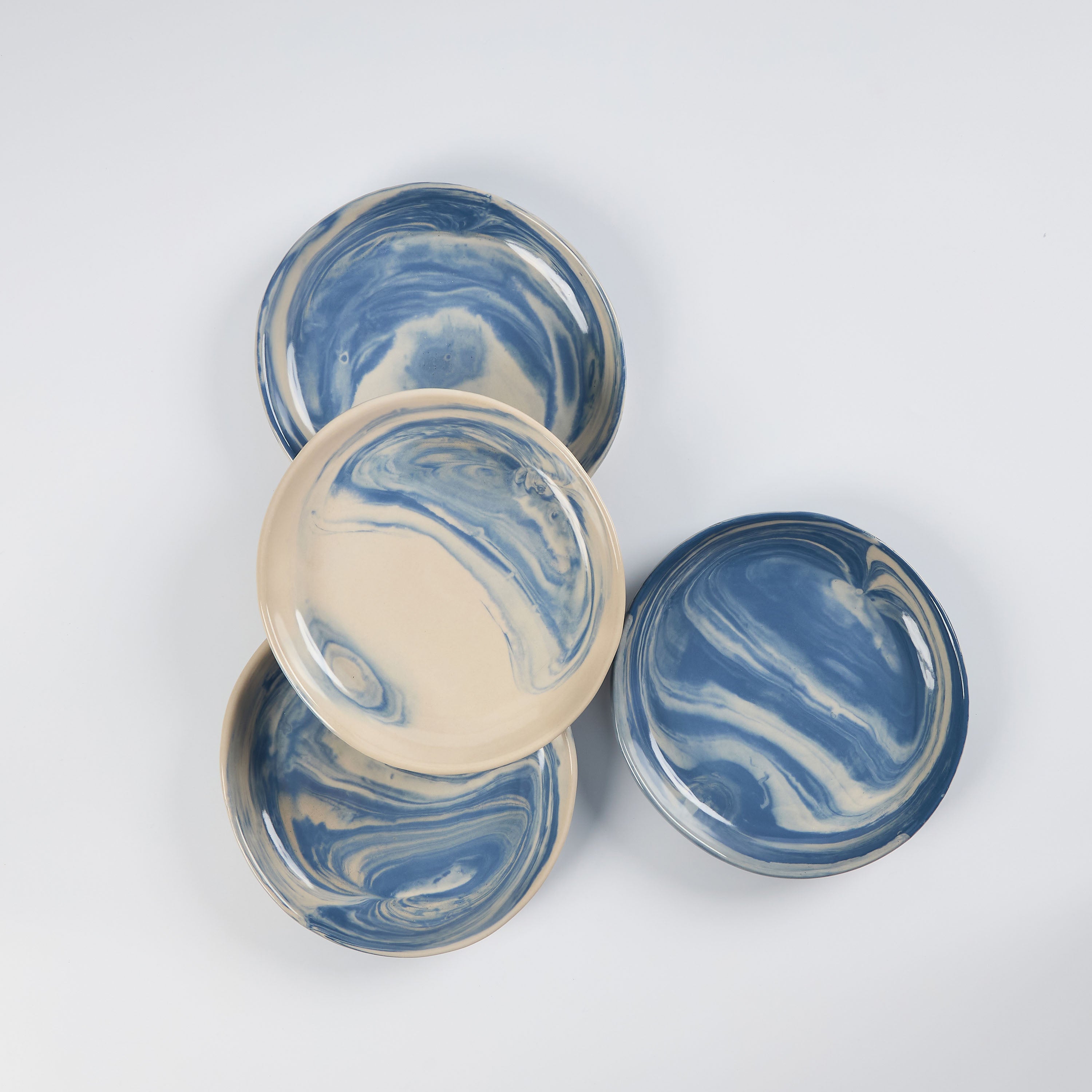 Set of four small handmade ceramic plates with a marbled clay pattern in cobalt blue, beige and cream on a white background by Palinopsia