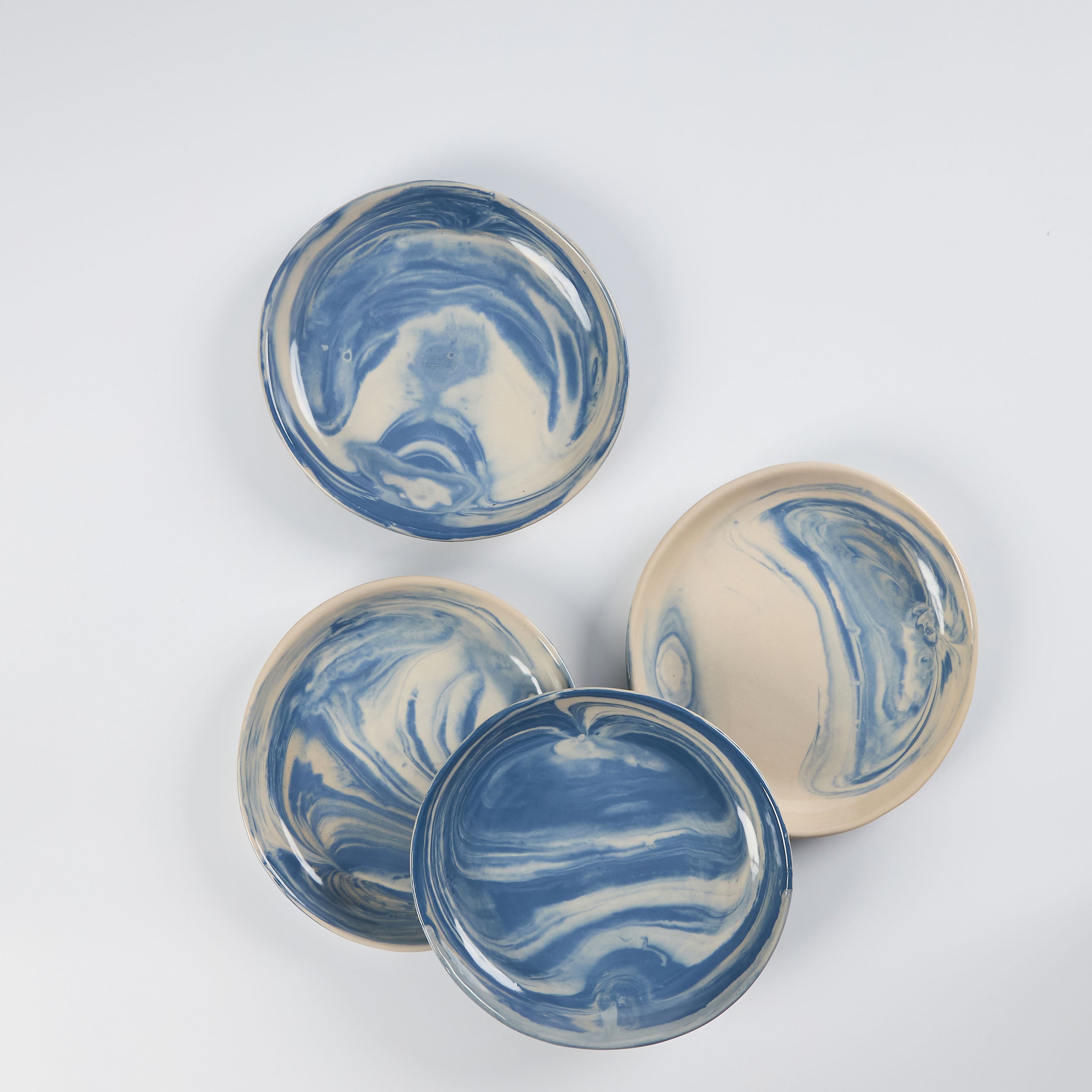 Set of four small handmade ceramic plates with a marbled clay pattern in cobalt blue, beige and cream on a white background by Palinopsia