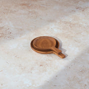 Two circular teak serving dishes with handles of different sizes stacked on a light stone background.