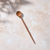 Bird’s-eye view of a Palinopsia long wooden teak spoon on a light stone background.