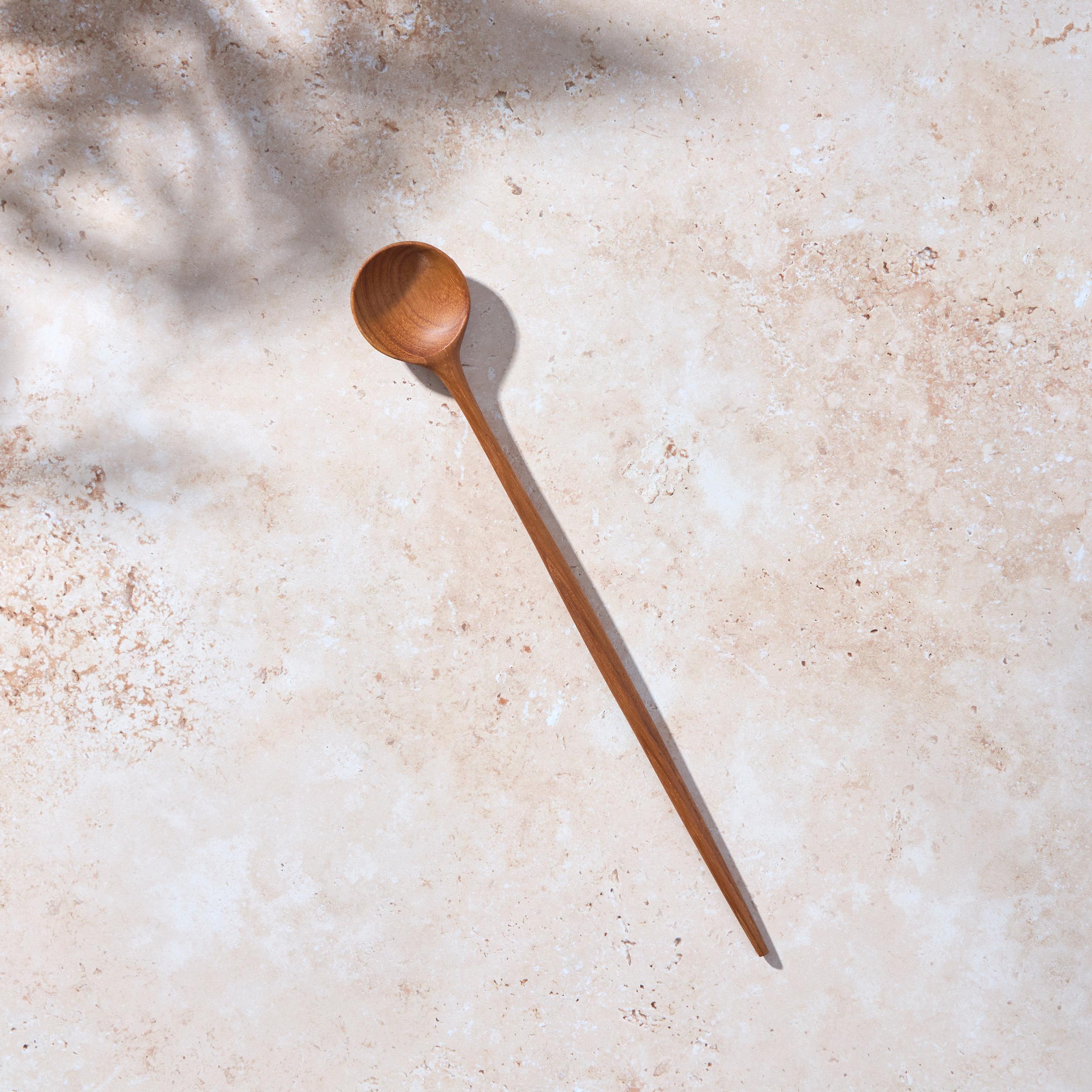 Bird’s-eye view of a Palinopsia long wooden teak spoon on a light stone background.