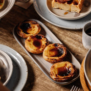 Rectangle ceramic dish with four Portuguese tarts on a breakfast table with a timber table top 