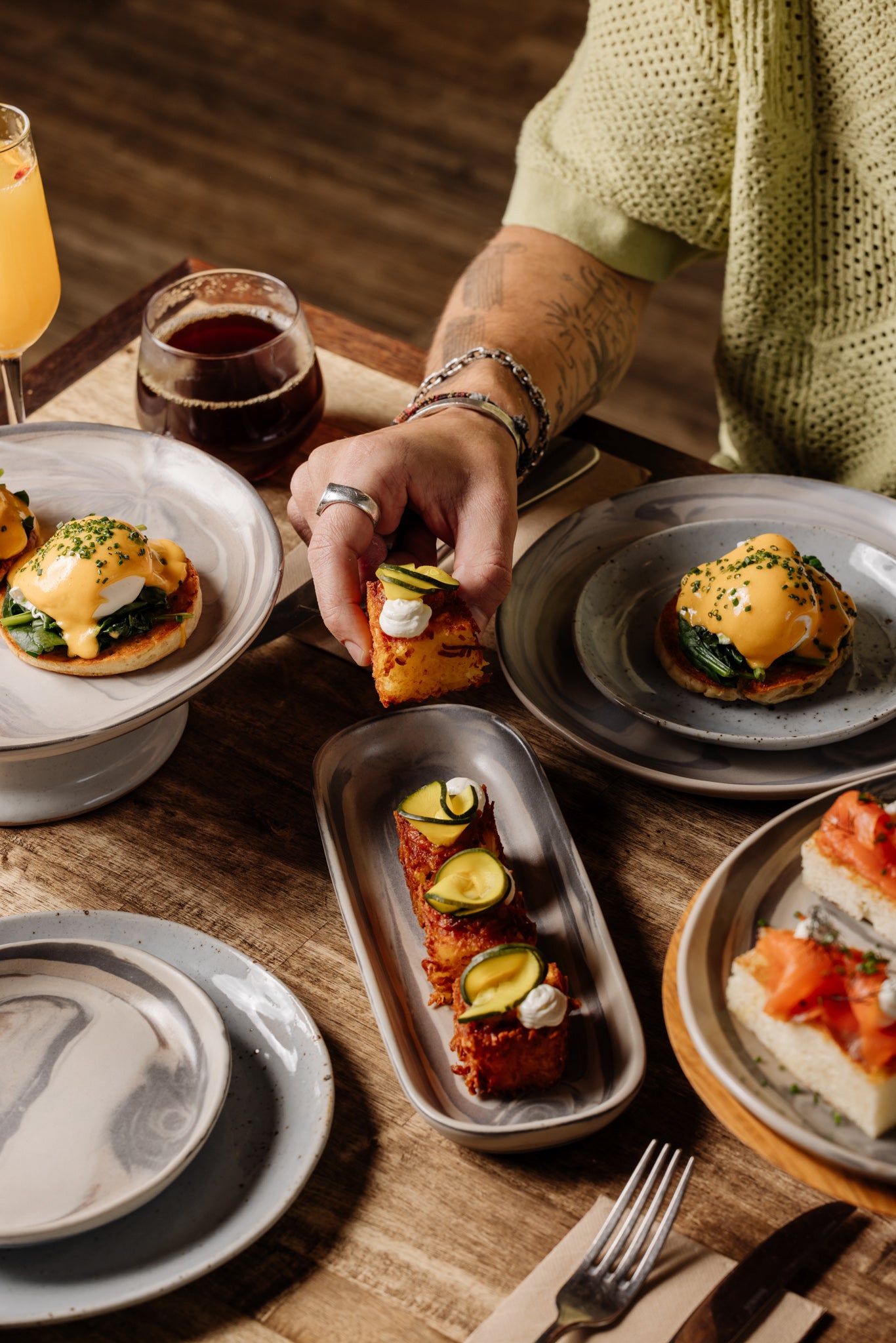Person enjoying a meal at a Newcastle cafe with plates of food served on handmade ceramics and drinks on a wooden table.