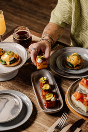 Person enjoying a meal at a Newcastle cafe with plates of food served on handmade ceramics and drinks on a wooden table.