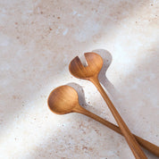 Angled shot of a retro teak wooden salad serving set by Palinopsia on a light stone background.