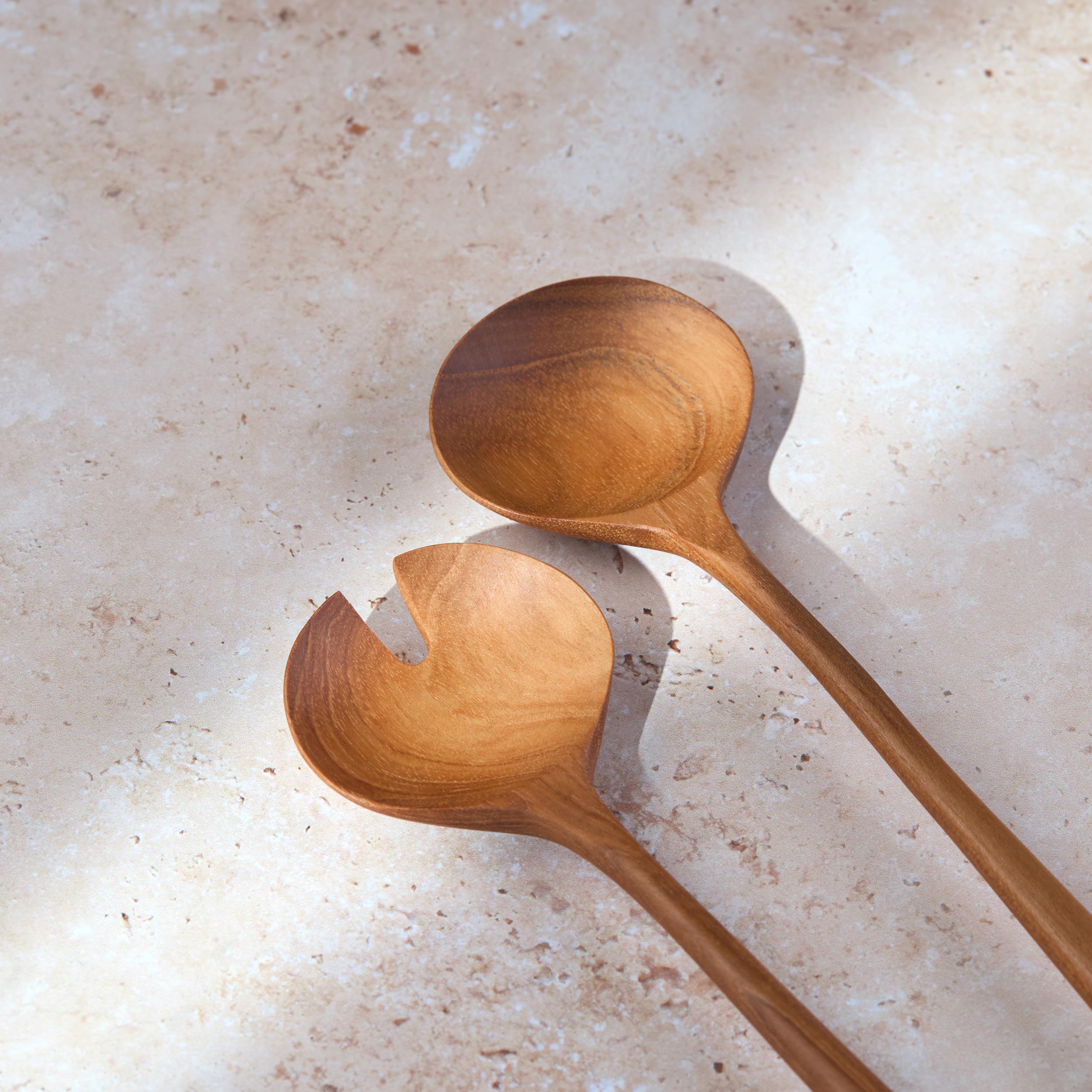 Detailed shot of a retro teak wooden salad serving set by Palinopsia on a light stone background.