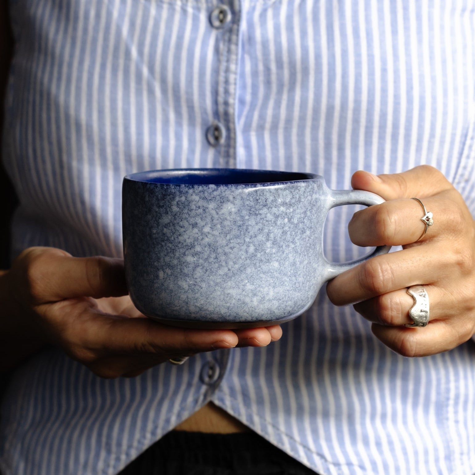 Woman holding a Palinopsia Ceramics mug resembling snow with dark midnight blue and white colours