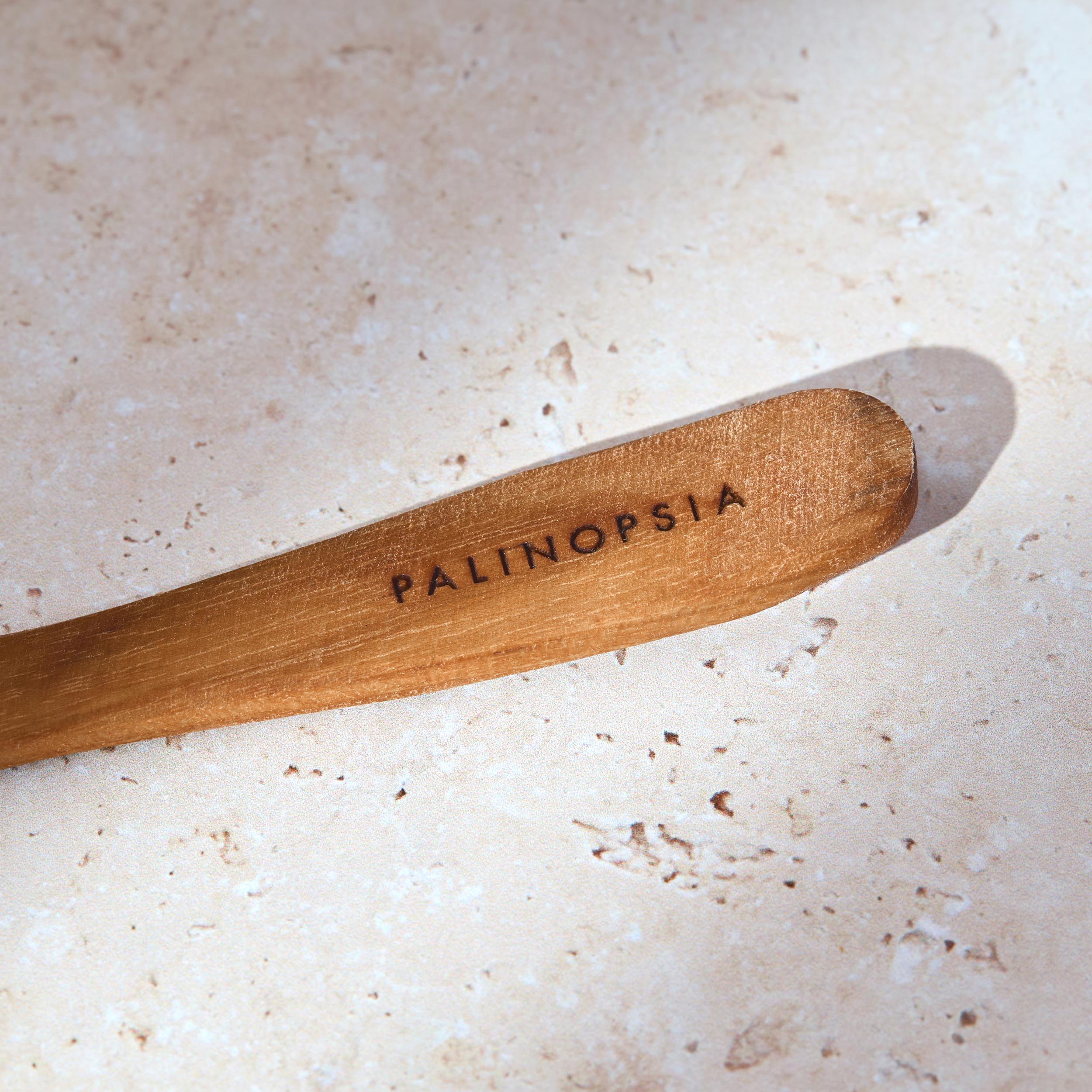 Close-up shot of the handle of a teak wooden breakfast spoon with a Palinopsia label on the handle.