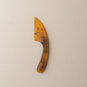 Small resin cheese knife in tortoise shell colours on a beige background