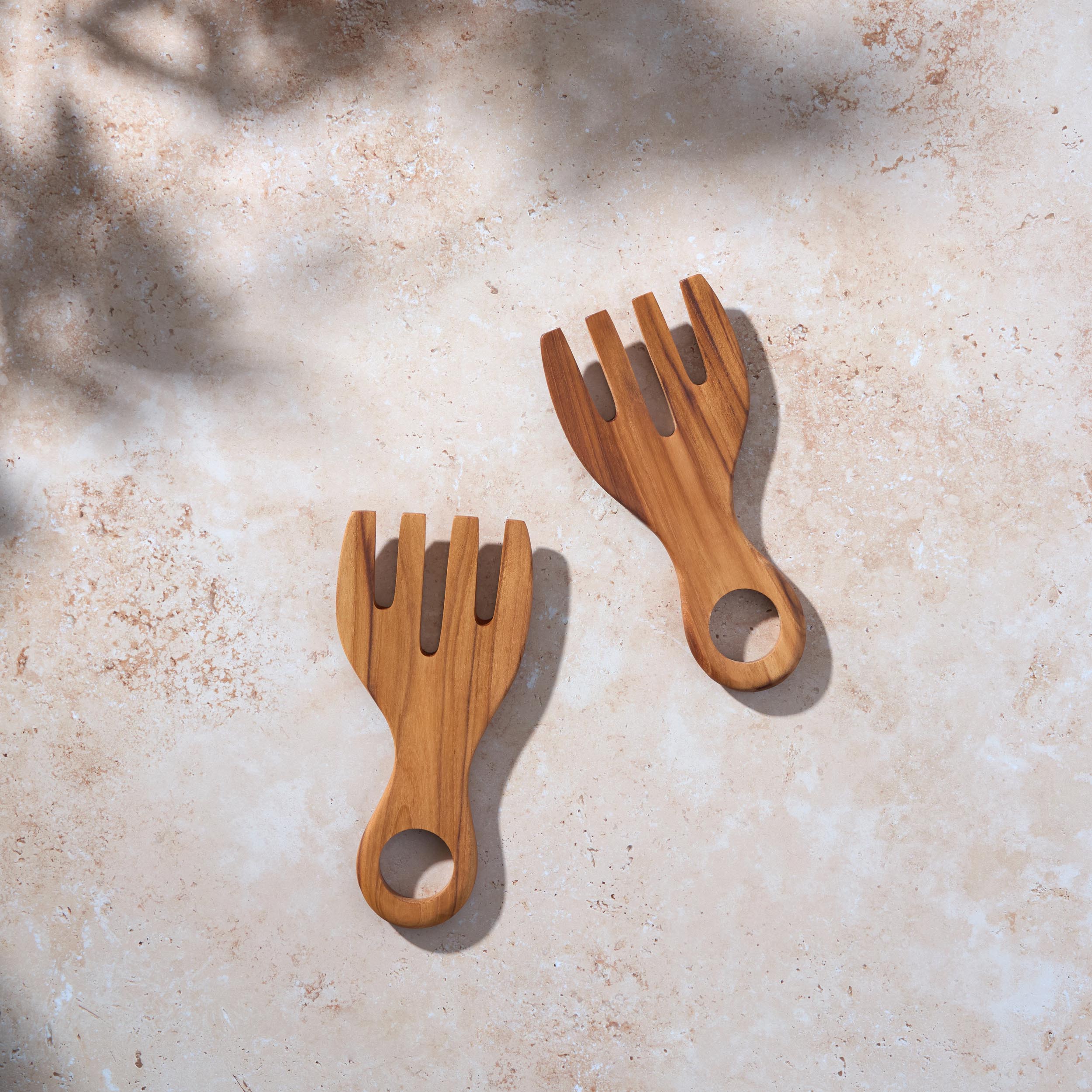 Bird’s-eye view of a set of chunky teak wooden salad serving forks on a light stone background.