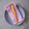 Lilac linen table napkin by Palinopsia Ceramics on a blue plate and a handmade olive wood butter knife
