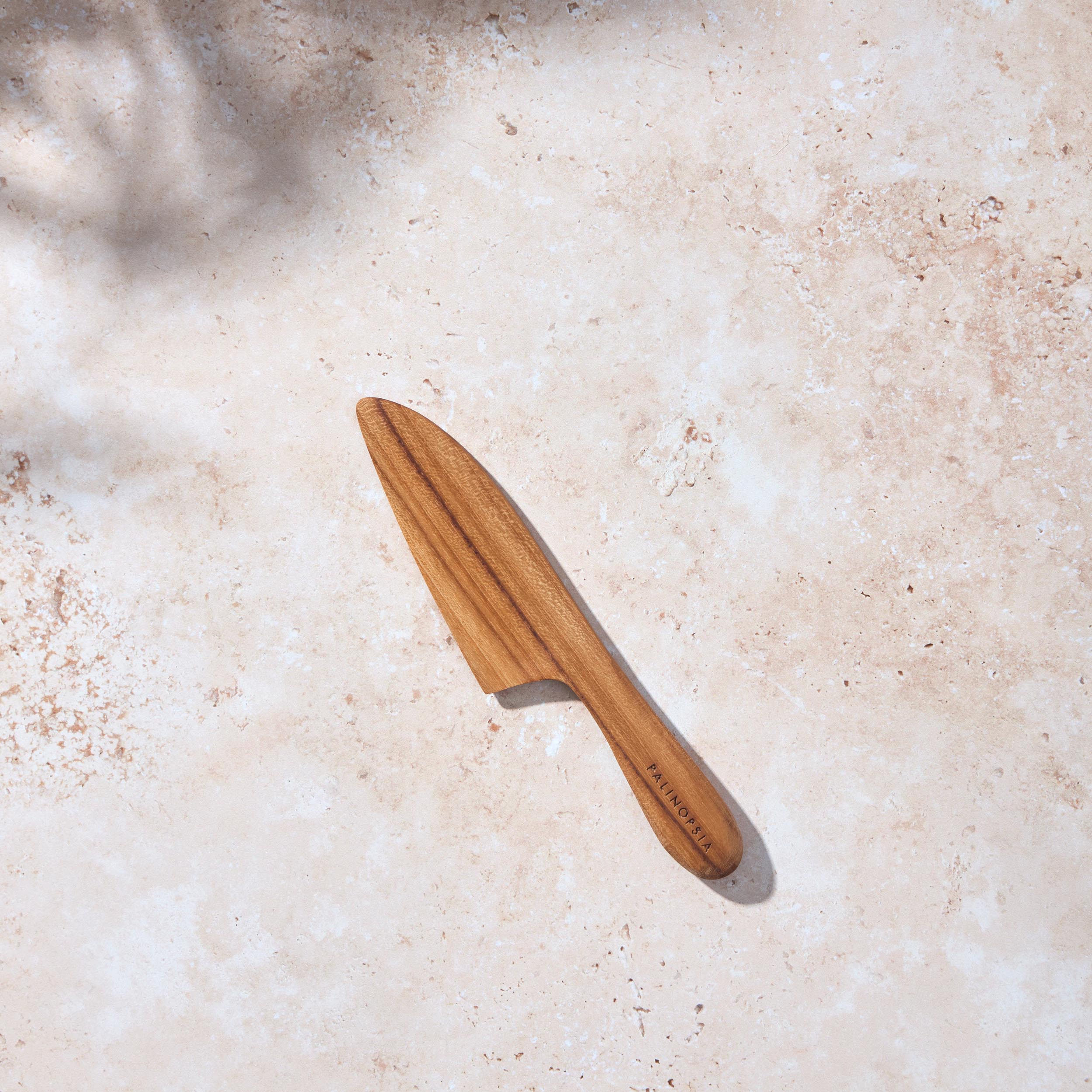 Bird’s-eye view of a Palinopsia wooden teak cheese knife on a light stone background.