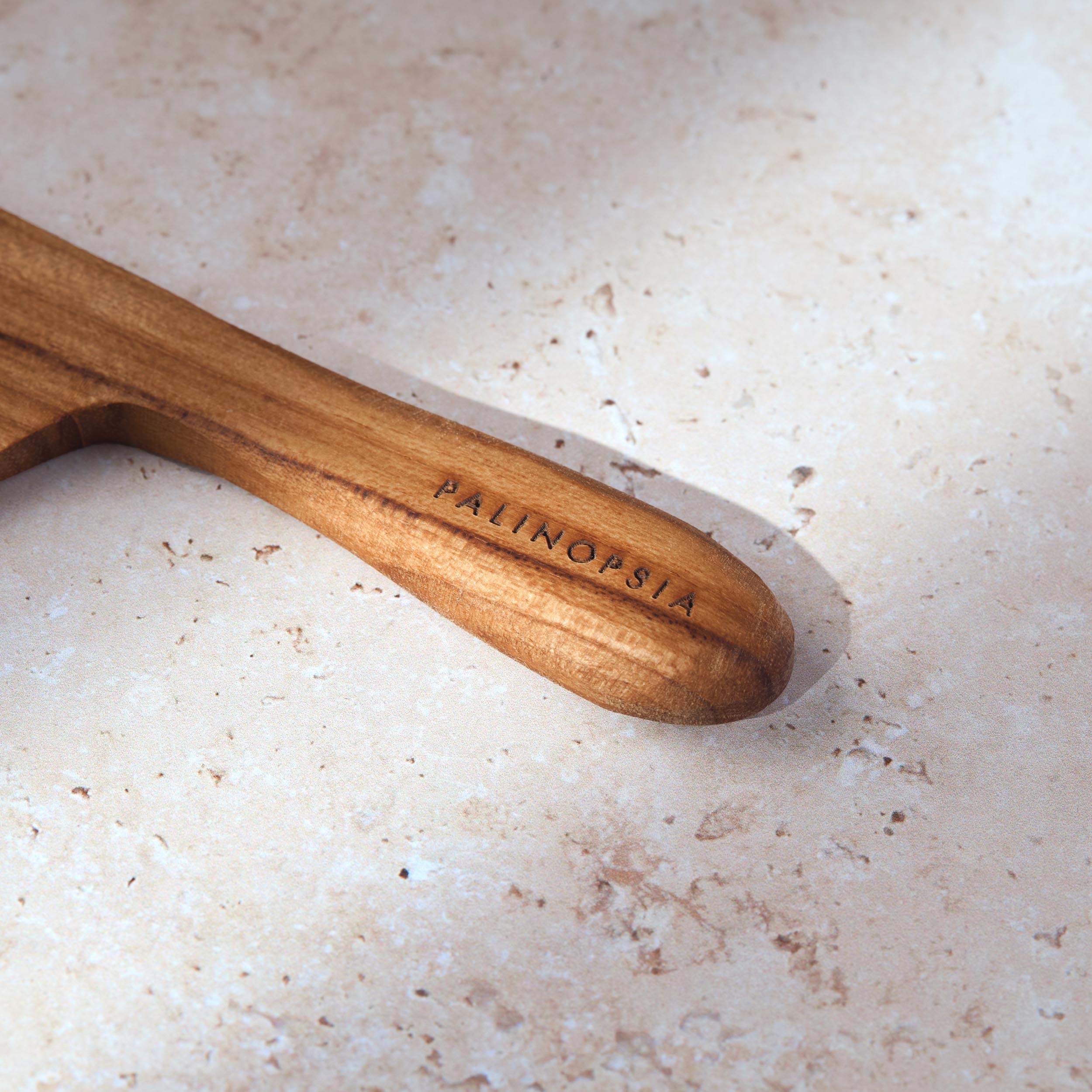 Close-up shot of the handle of a teak wooden board cheese knife with a Palinopsia label on the handle.