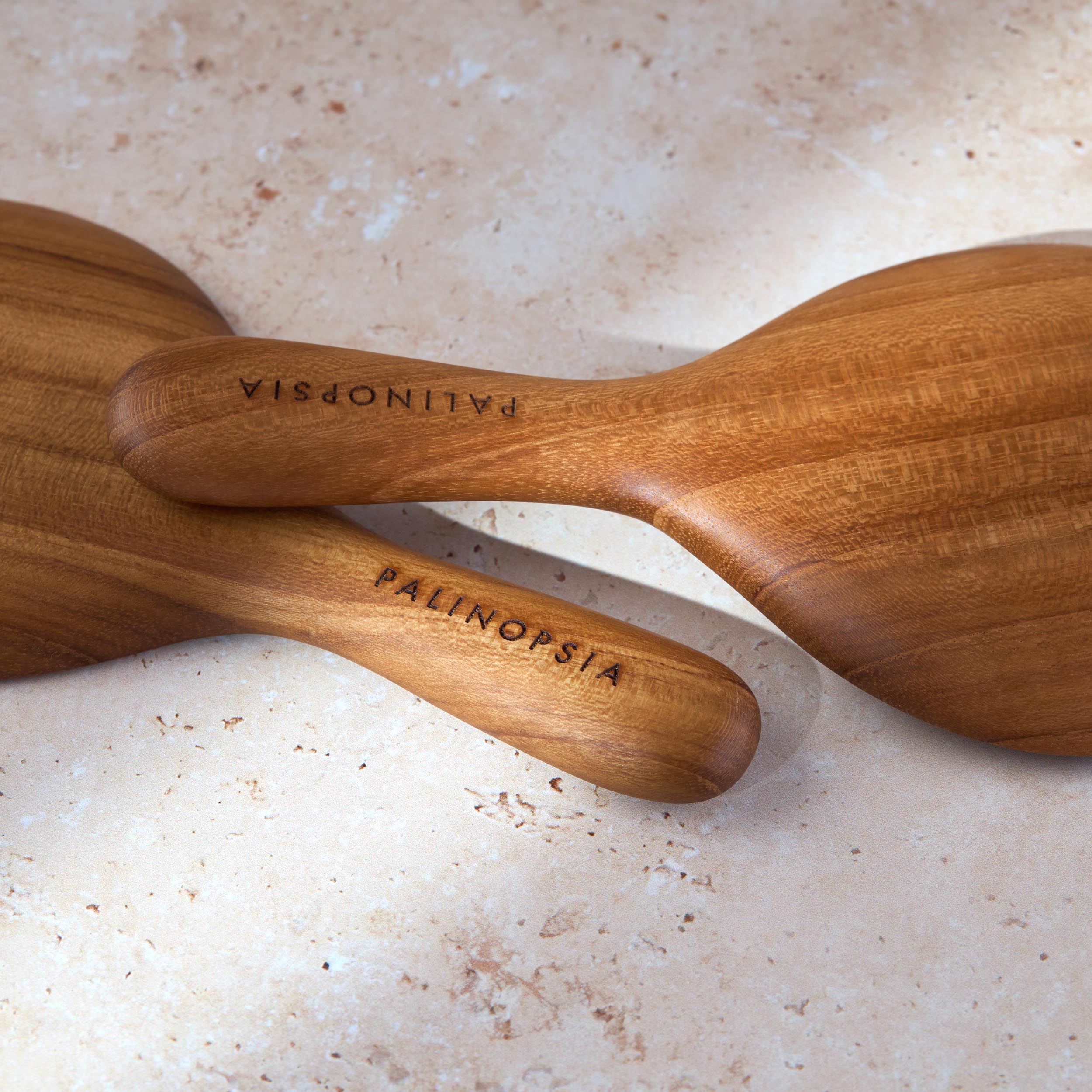 Close-up shot of the handles of short teak wooden salad servers with Palinopsia labels on the handles.