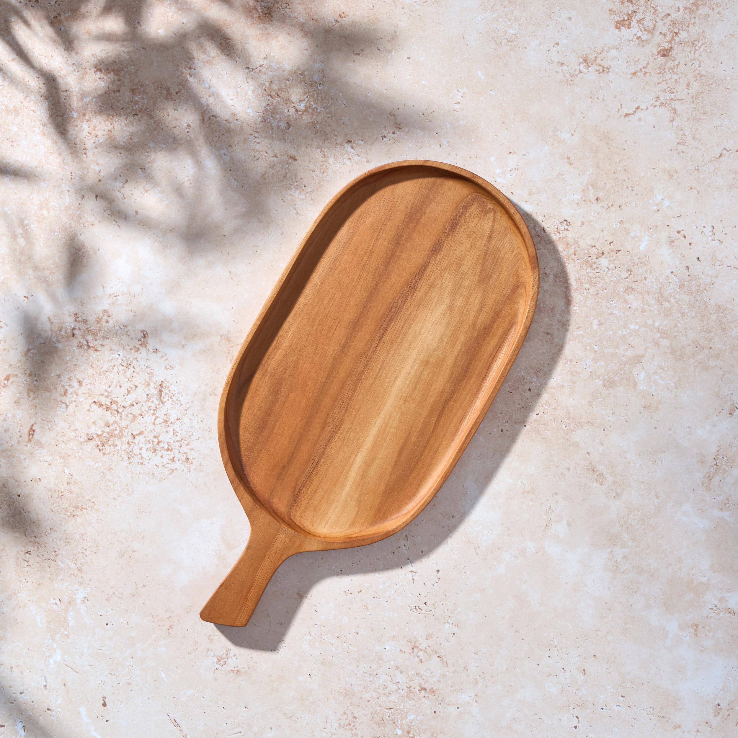 Bird’s-eye view of a Palinopsia teak wooden rectangular serving platter cheese board with a handle on a light stone background. 