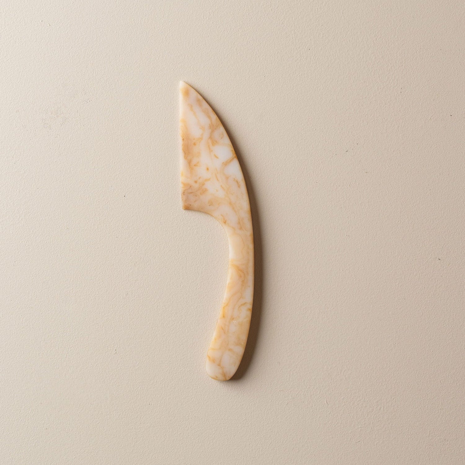 Decorative resin cheese knife on a beige background white and coffee coloured