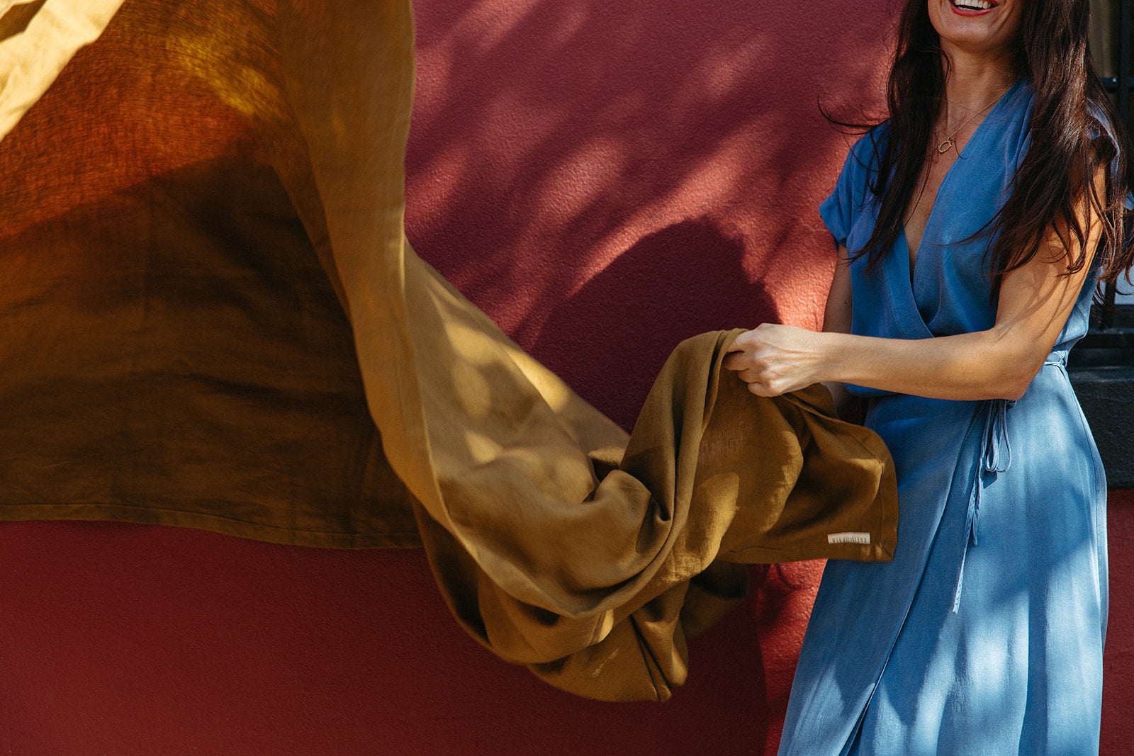 Woman in blue dress holding an olive linen tablecloth 