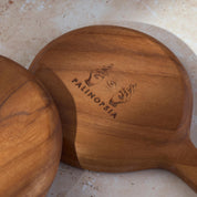 Detailed shot of two teak wooden serving dishes with the Palinopsia logo on the bottom.
