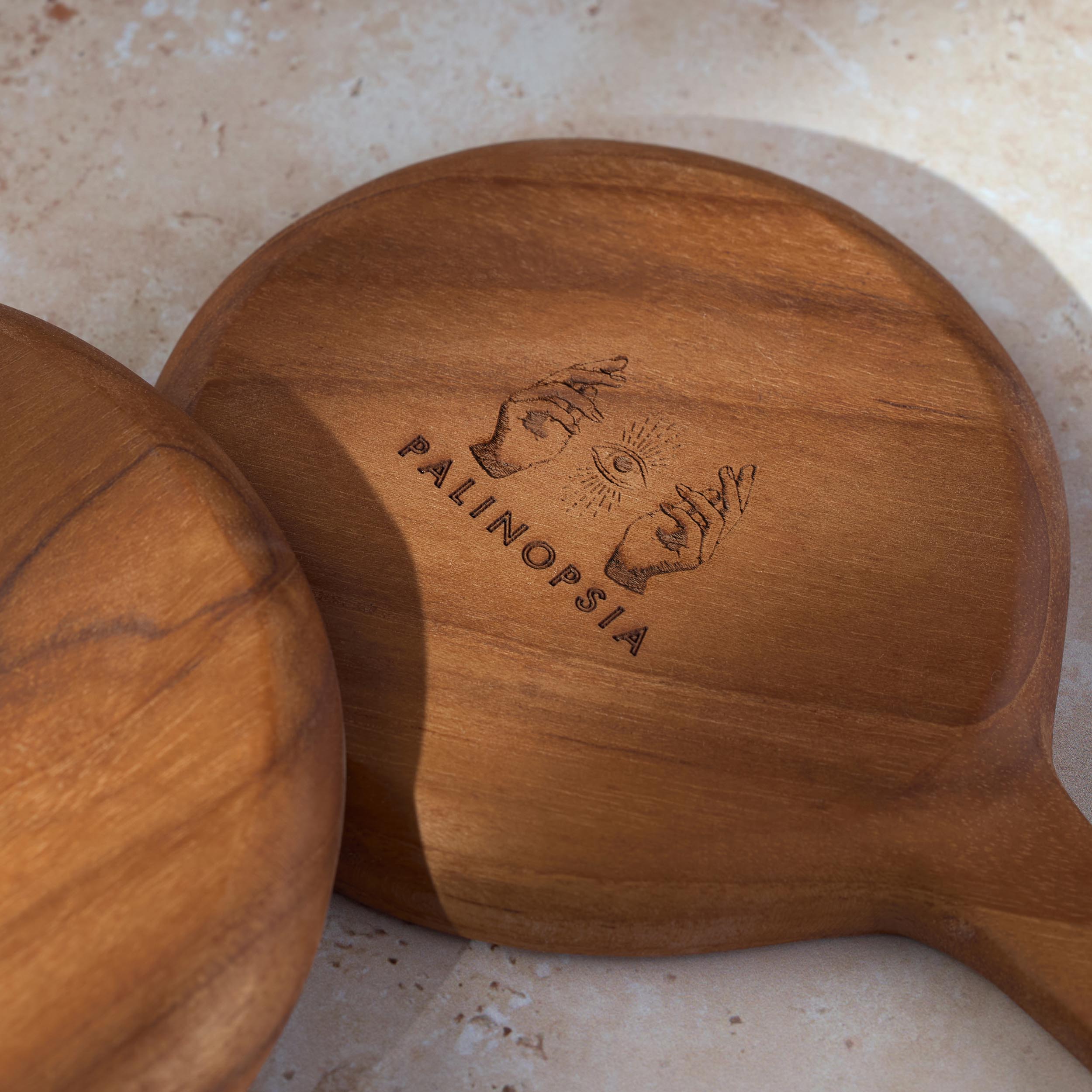 Detailed shot of two teak wooden serving dishes with the Palinopsia logo on the bottom.