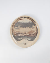 Round ceramic plate with landscape design on a white background
