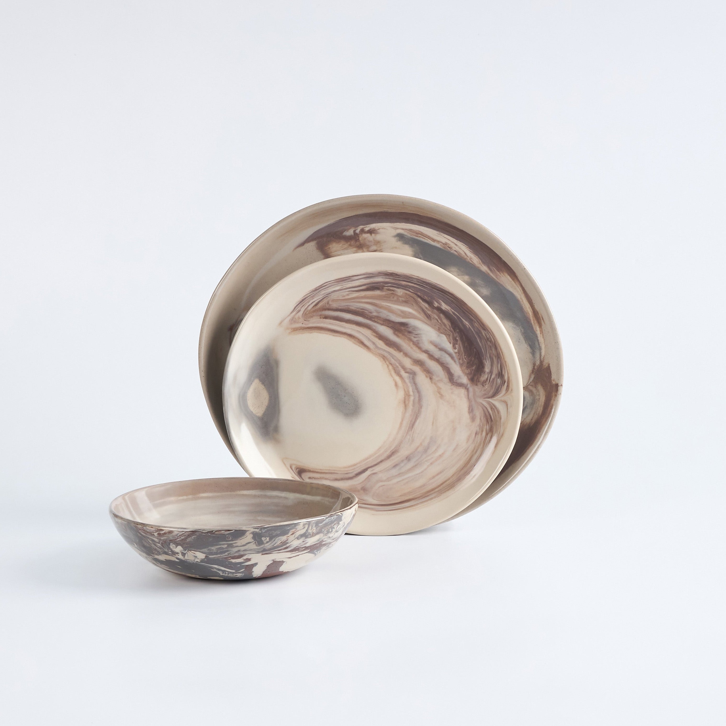 Three piece dinner set in marbled clay, earthy neutral tones on a white background. 