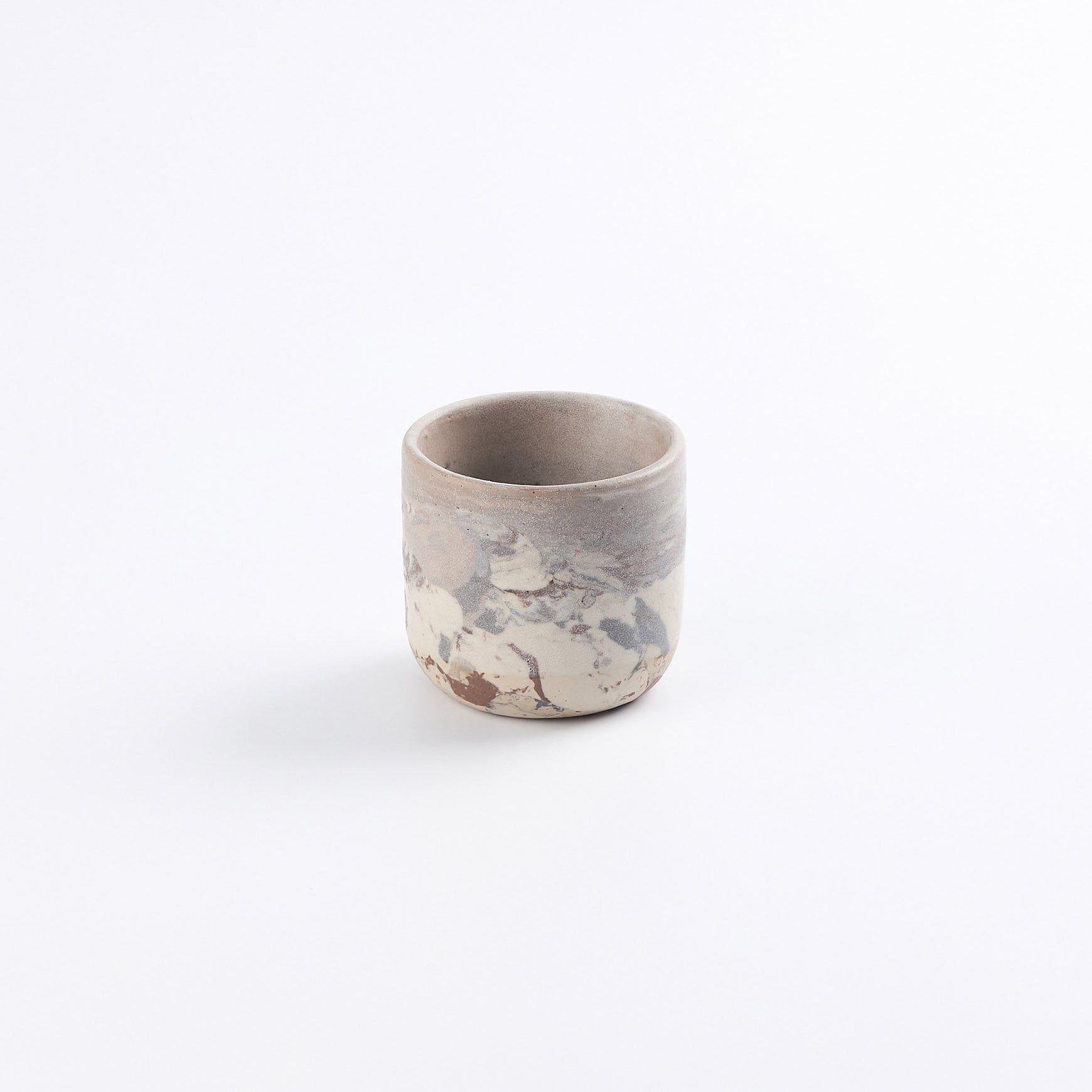 Petite ceramic stoneware cup with abstract marble design of mixed clays; red, black, sandstone, white and a matte white glaze on a white background