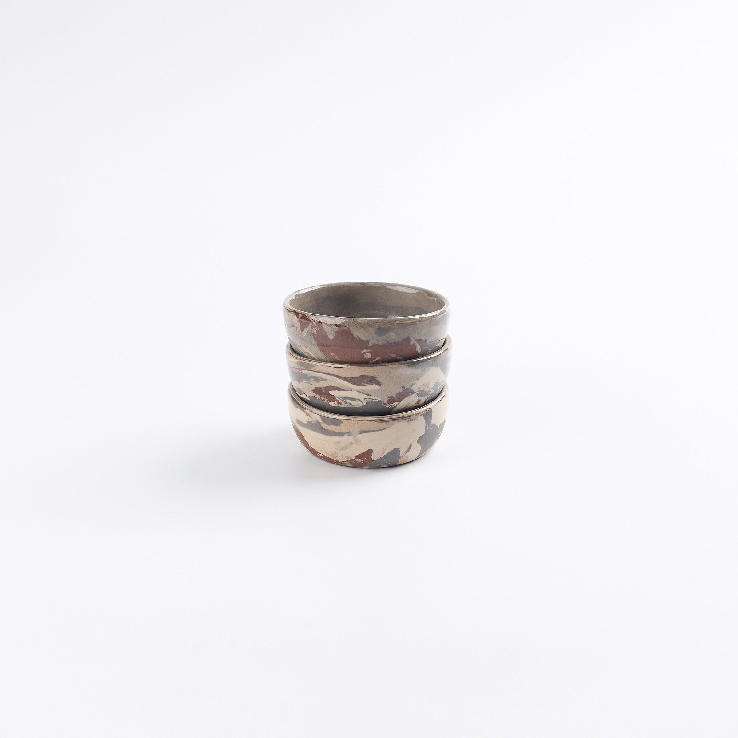 Stack of marbled ceramic small dishes with earthy tones on a white background