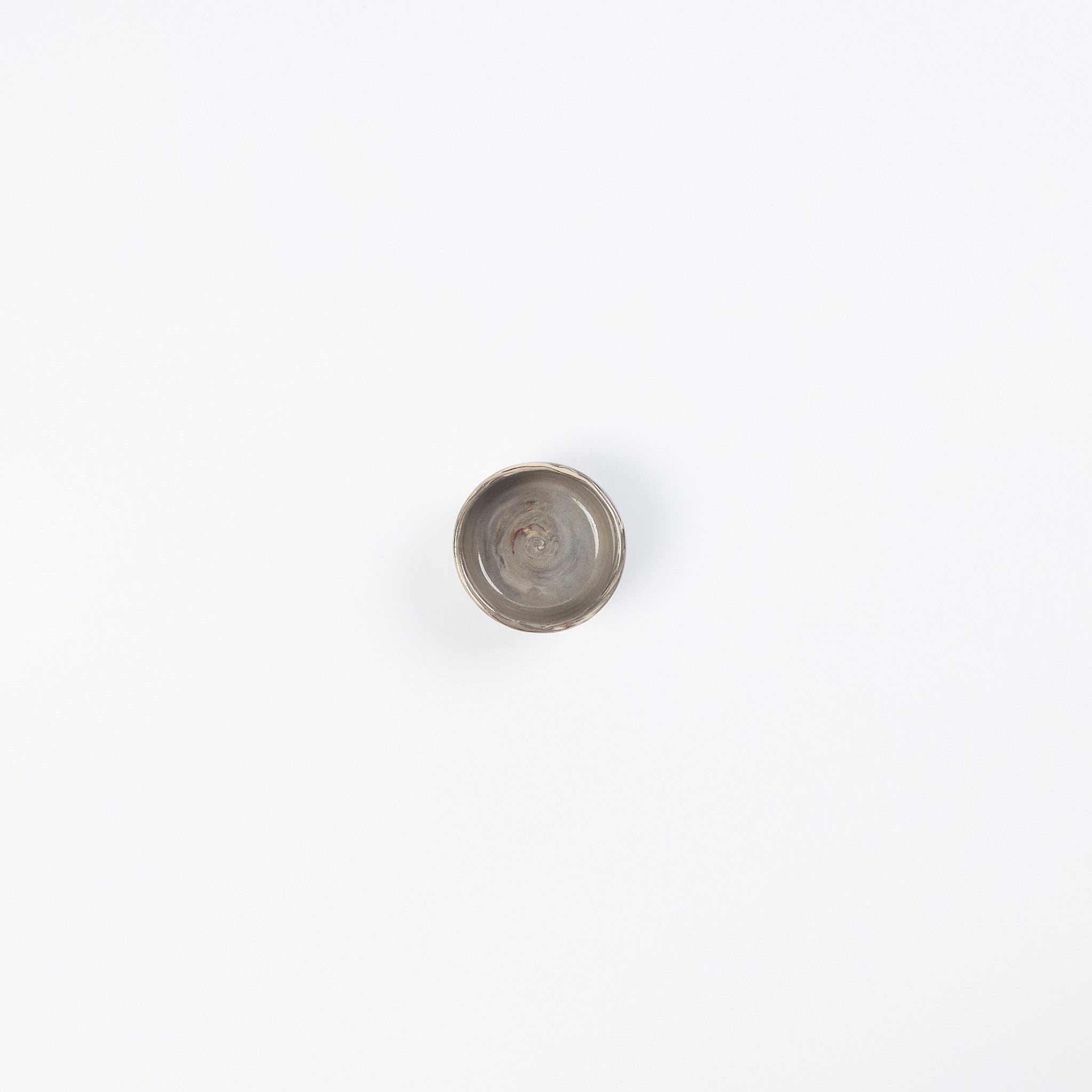 Birds eye view of a small ceramic salt dish in neutral colours on white background 