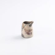 Small ceramic hand pourer pitcher with marbled design on a white background