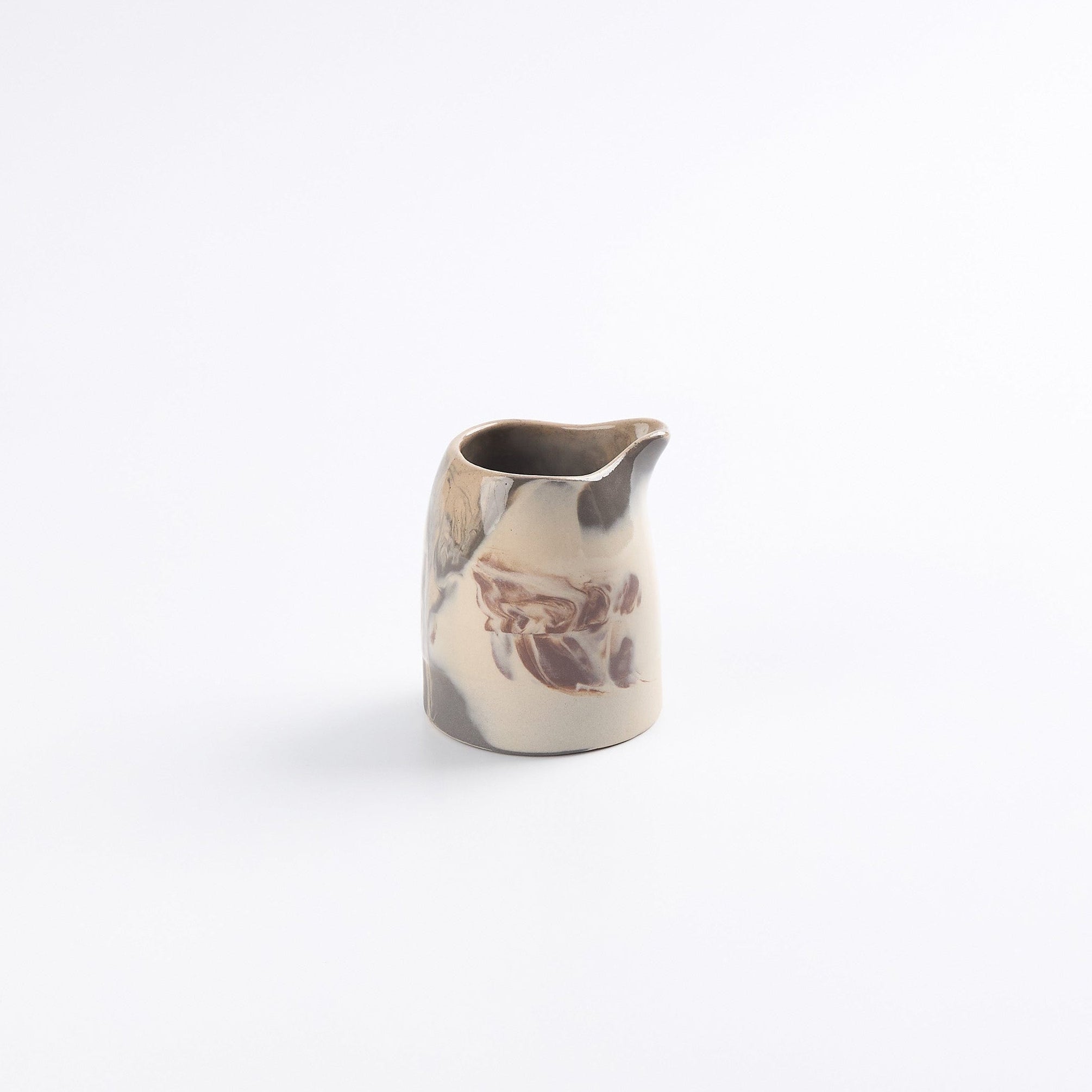Small ceramic hand pourer pitcher with marbled design on a white background